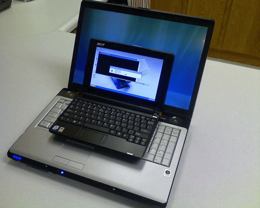 A black laptop positioned on top of a larger silver laptop, both showing computer screens with a login prompt and desktop backgrounds.