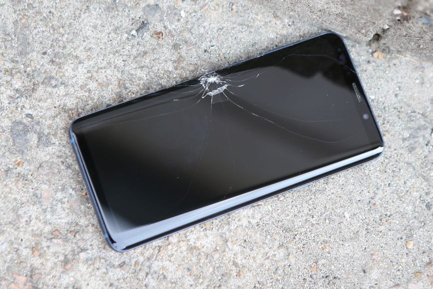 A smartphone with a cracked screen lying on a concrete surface.
