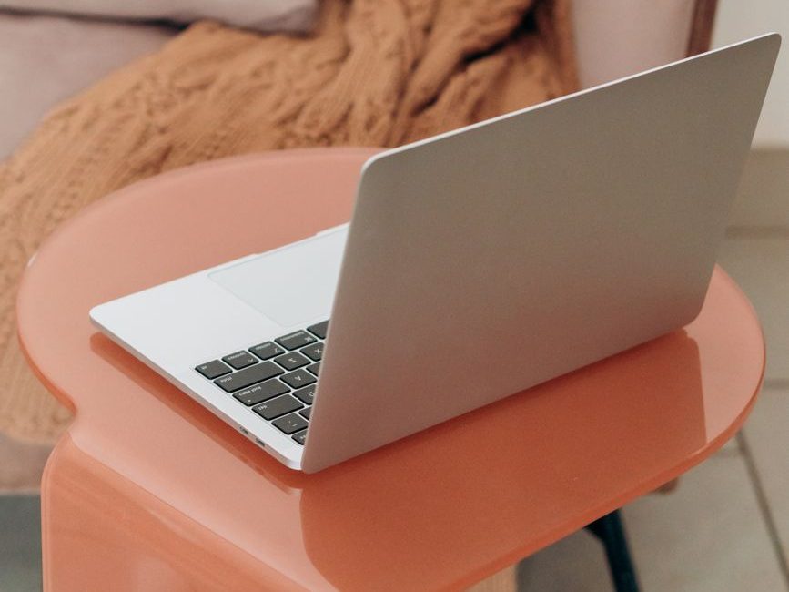 A silver laptop resting on a transparent orange table, with a cozy knitted blanket in the background.