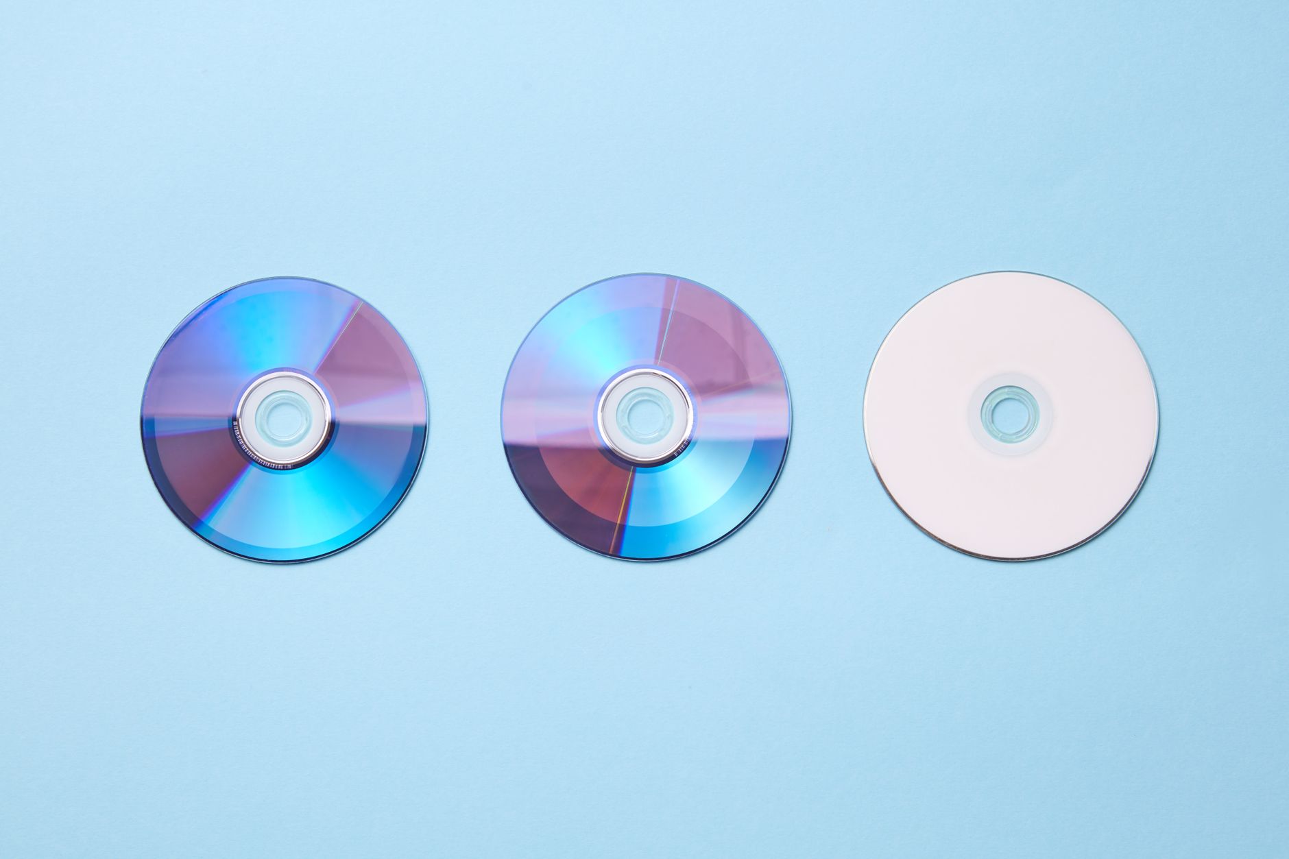 Three CDs displayed on a light blue background, including two reflective discs and one blank disc.